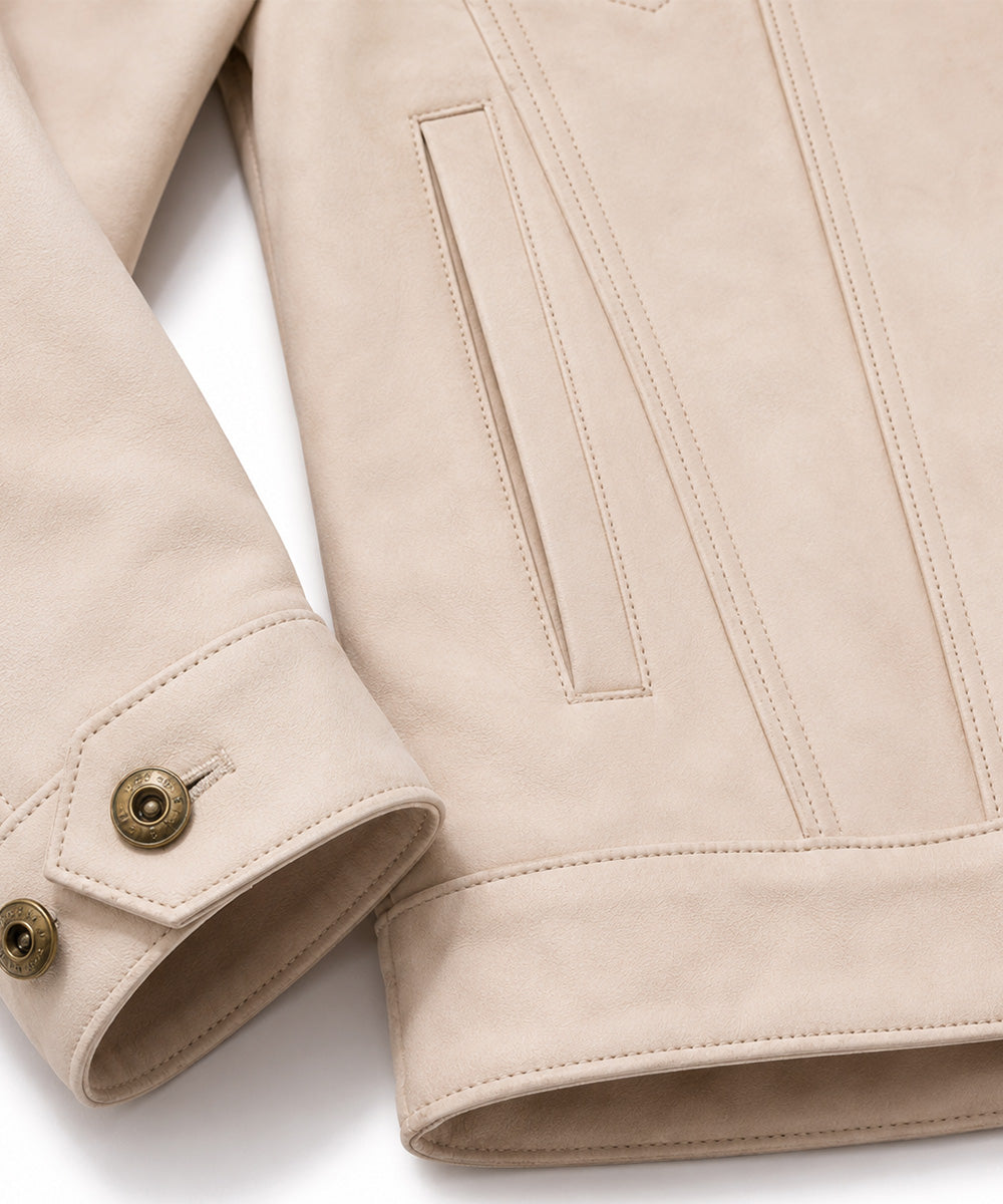 Close-up of a light beige suede jacket showing the sleeve cuff with two brass buttons and a vertical welt pocket on the chest.