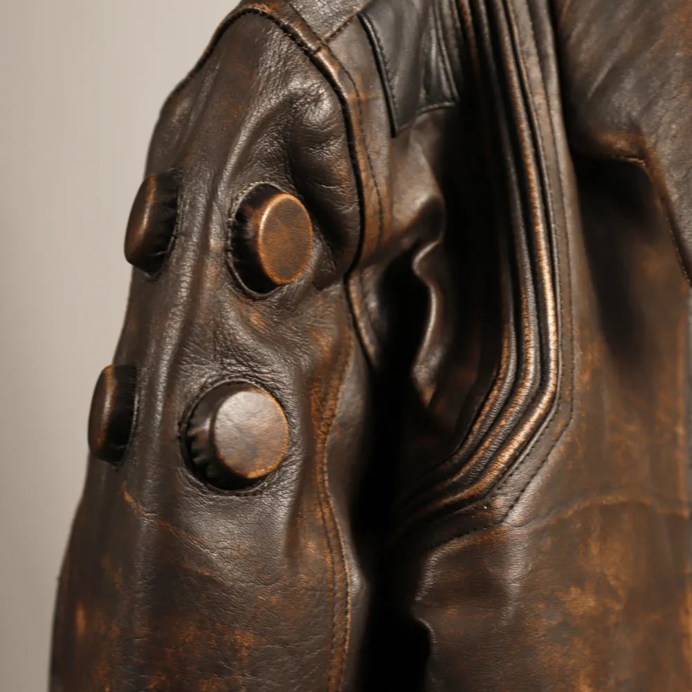 Close-up of a distressed brown leather jacket featuring large round metallic buttons on the shoulder and sleeve, with detailed stitching and a textured leather surface.
