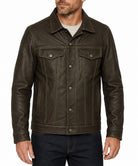A man wearing a dark brown leather jacket with a button-up front, chest flap pockets, and contrast stitching, paired with a light gray t-shirt and dark blue jeans, against a plain white background.