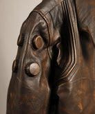 Close-up of a distressed brown leather jacket featuring large round metallic buttons on the shoulder and sleeve, with detailed stitching and a textured leather surface.