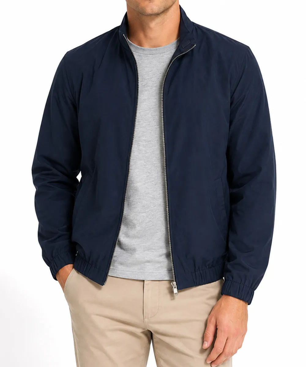 A man wearing a navy blue zip-up bomber jacket over a light gray t-shirt and khaki pants, shown from the chin down against a plain white background.