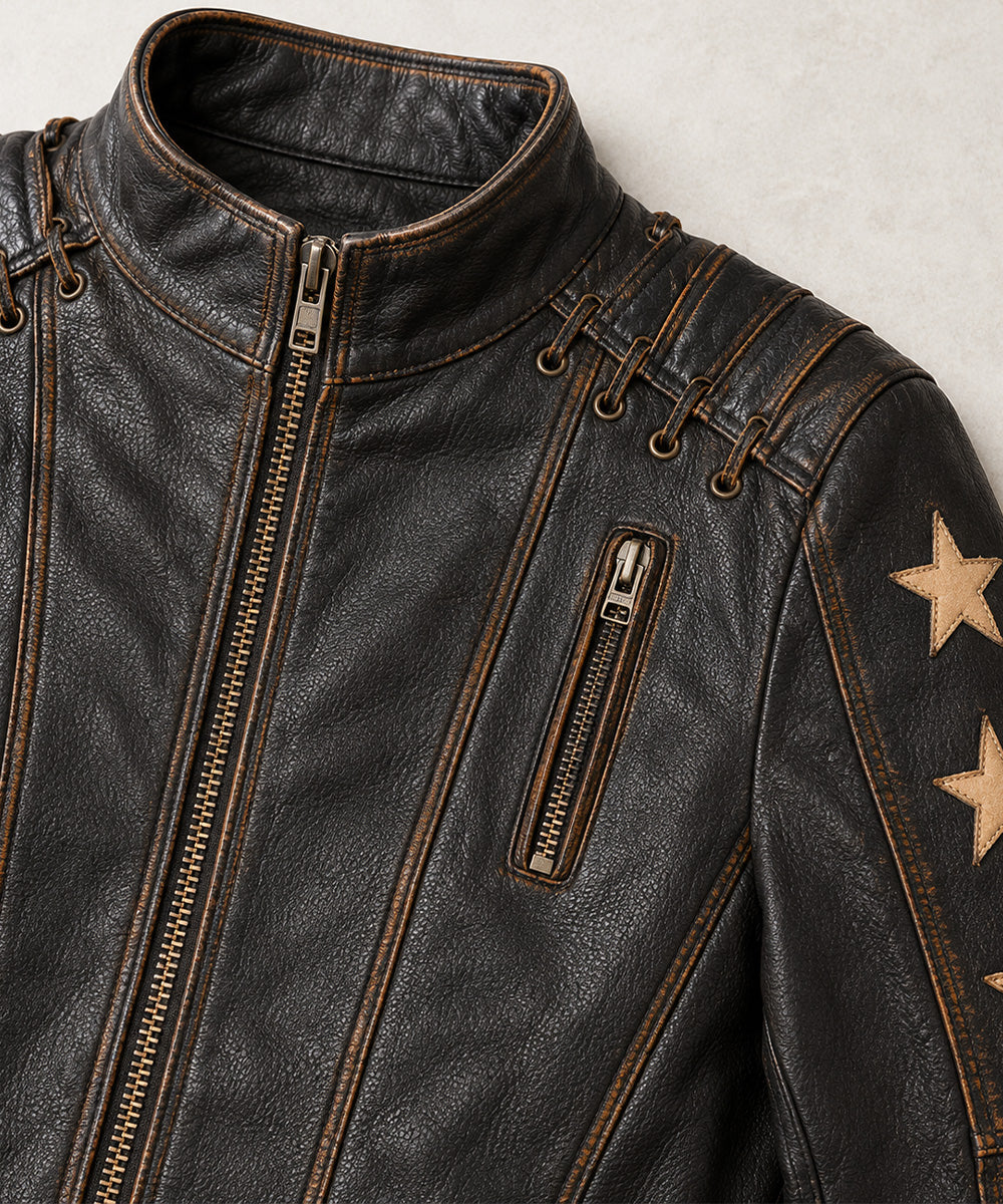 Close-up of a dark brown distressed leather jacket with gold-toned zippers, contrast stitching, and gold star patches on the sleeve, shown against a light textured background.